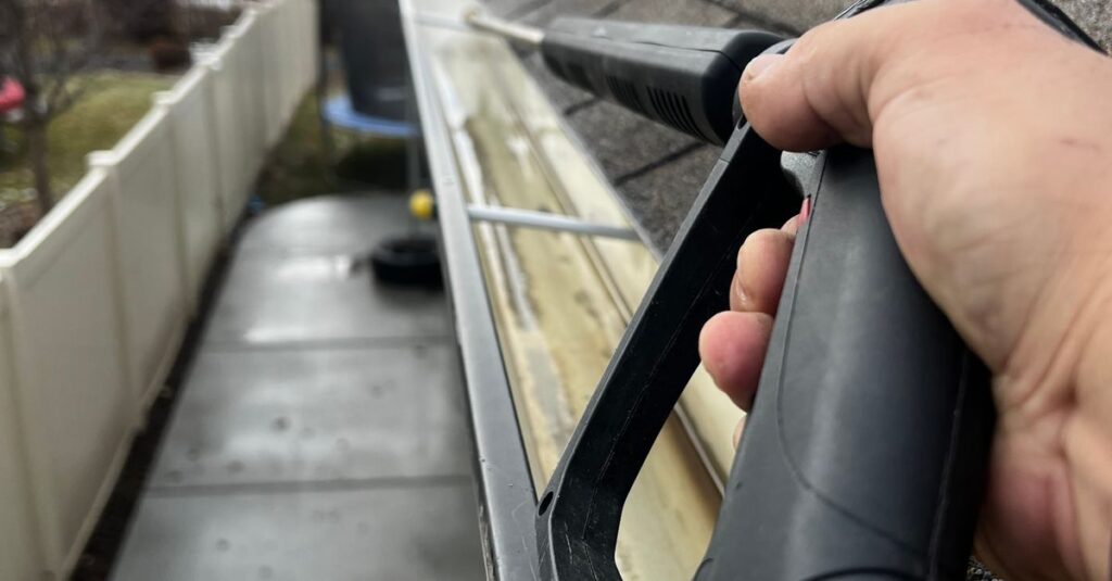 Close-up of gutter cleaning with pressure washer, outdoors, during the day.